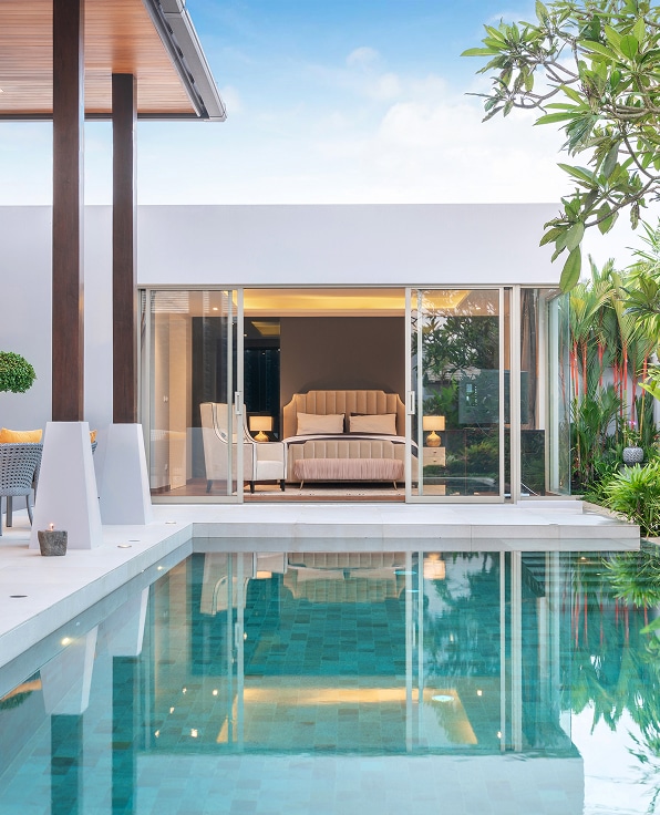 Chambre de villa luxueuse et moderne avec lit double, ouverte sur une piscine turquoise scintillante et une terrasse verdoyante.
