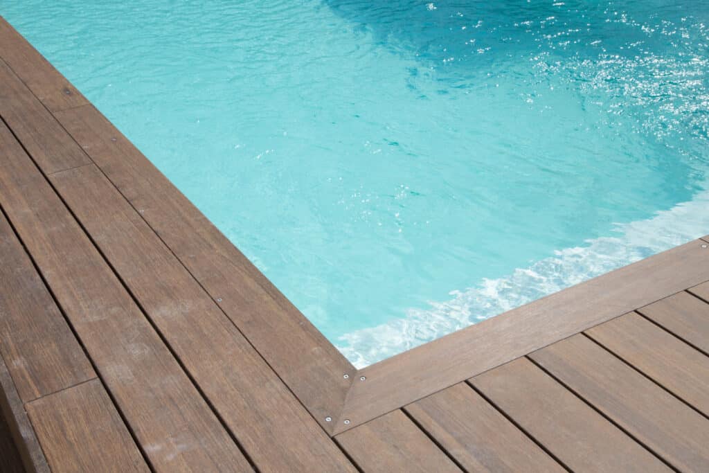 Piscine moderne à l'eau turquoise scintillante, bordée par une terrasse en bois foncé. Reflets de soleil sur l'eau claire.